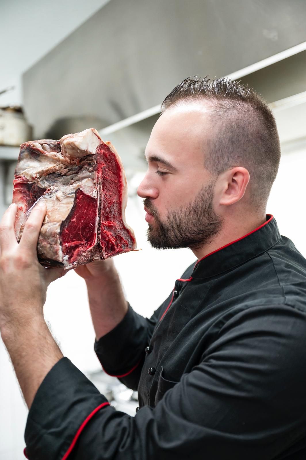Uno chef che annusa una grande bistecca frollata a secco in una cucina professionale.