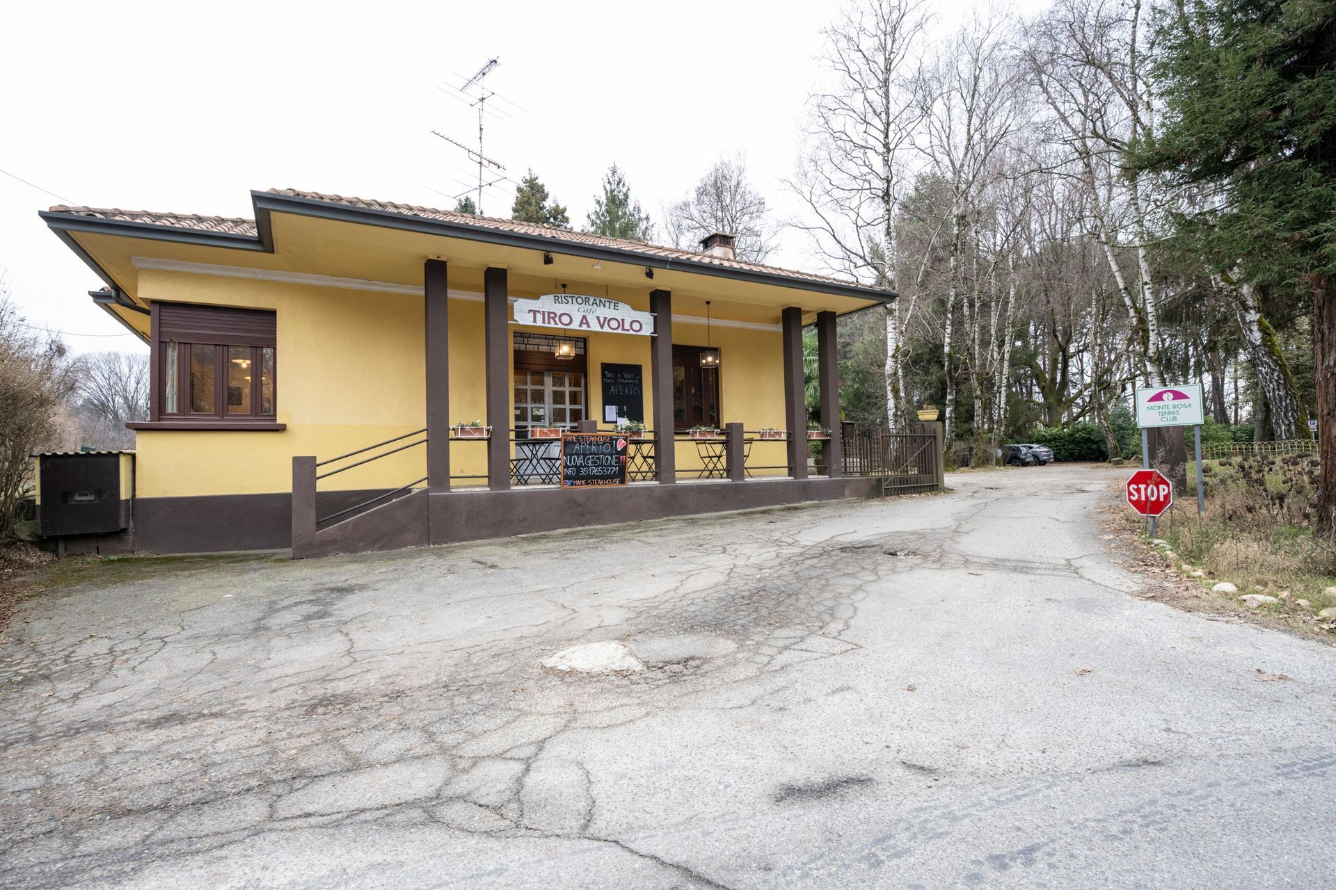 Interno del ristorante: tavoli in legno con apparecchiati, sedie scure, grandi finestre, pareti beige, luci a filo e disegni decorativi.