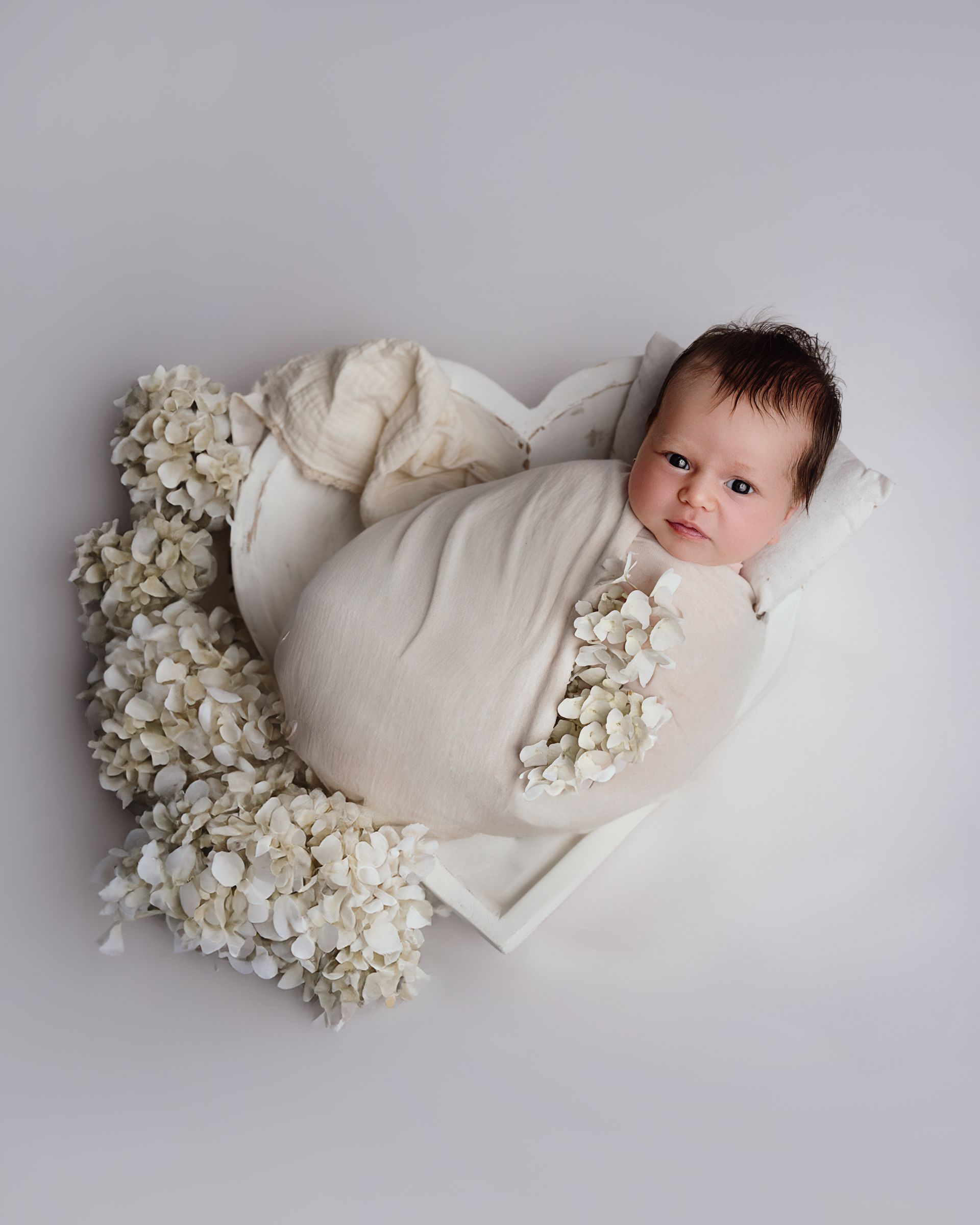 Le bébé porte une couronne de fleurs et tient un lapin en peluche.