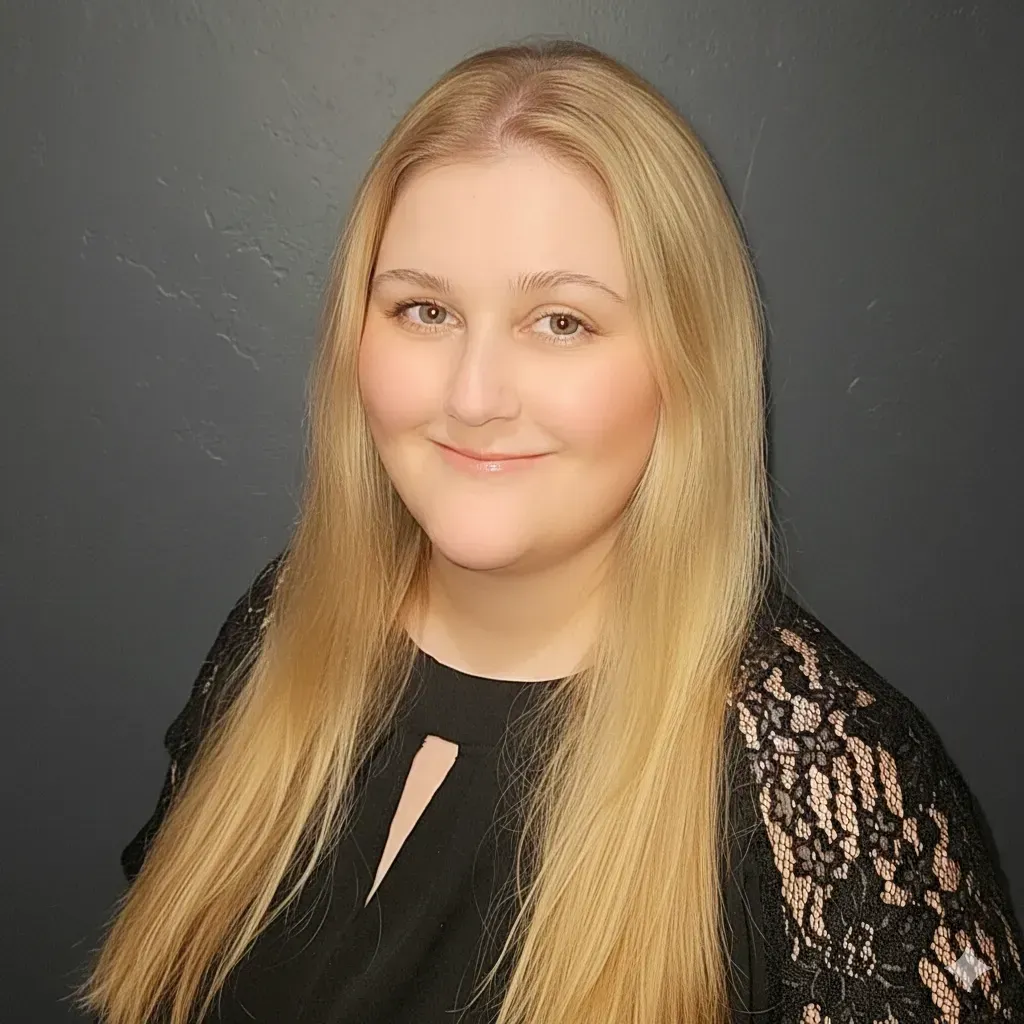 A person with long, light-colored hair and a gentle smile, wearing a black shirt with lace sleeves against a dark background.
