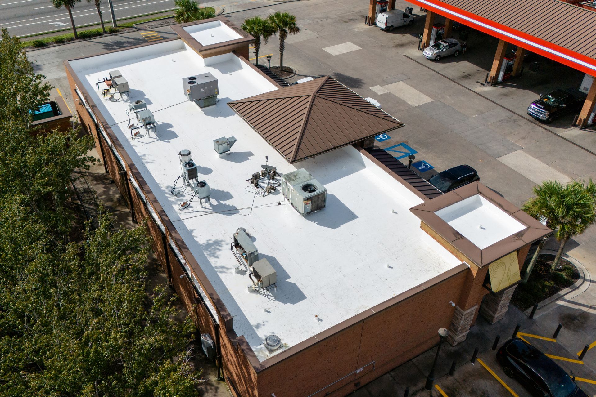 Aerial view of a single-story home with a dark gray shingled roof, white exterior, front porch, and a concrete driveway.
