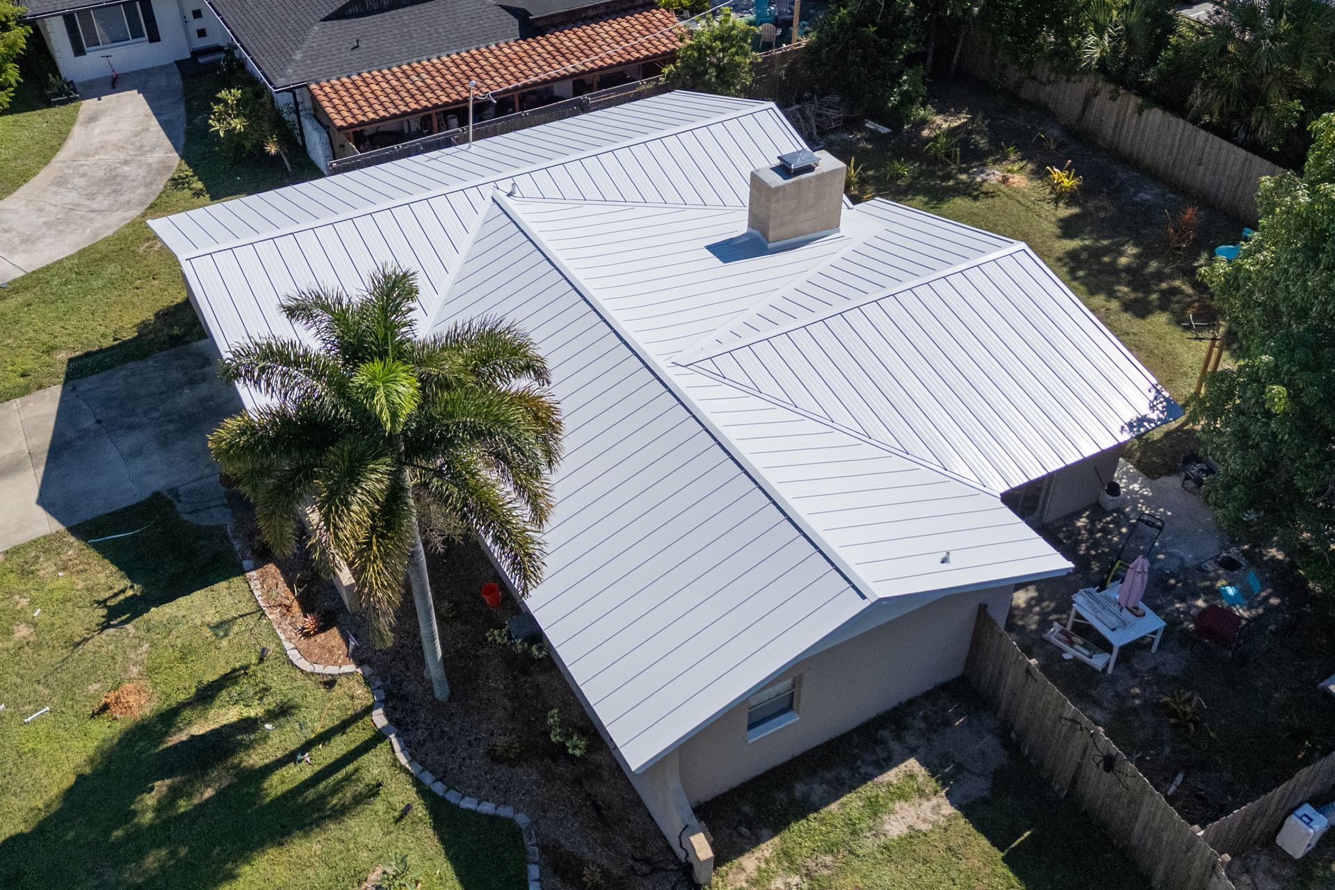 Aerial view of a white community center with a large green metal roof, surrounded by a lawn and palm trees.