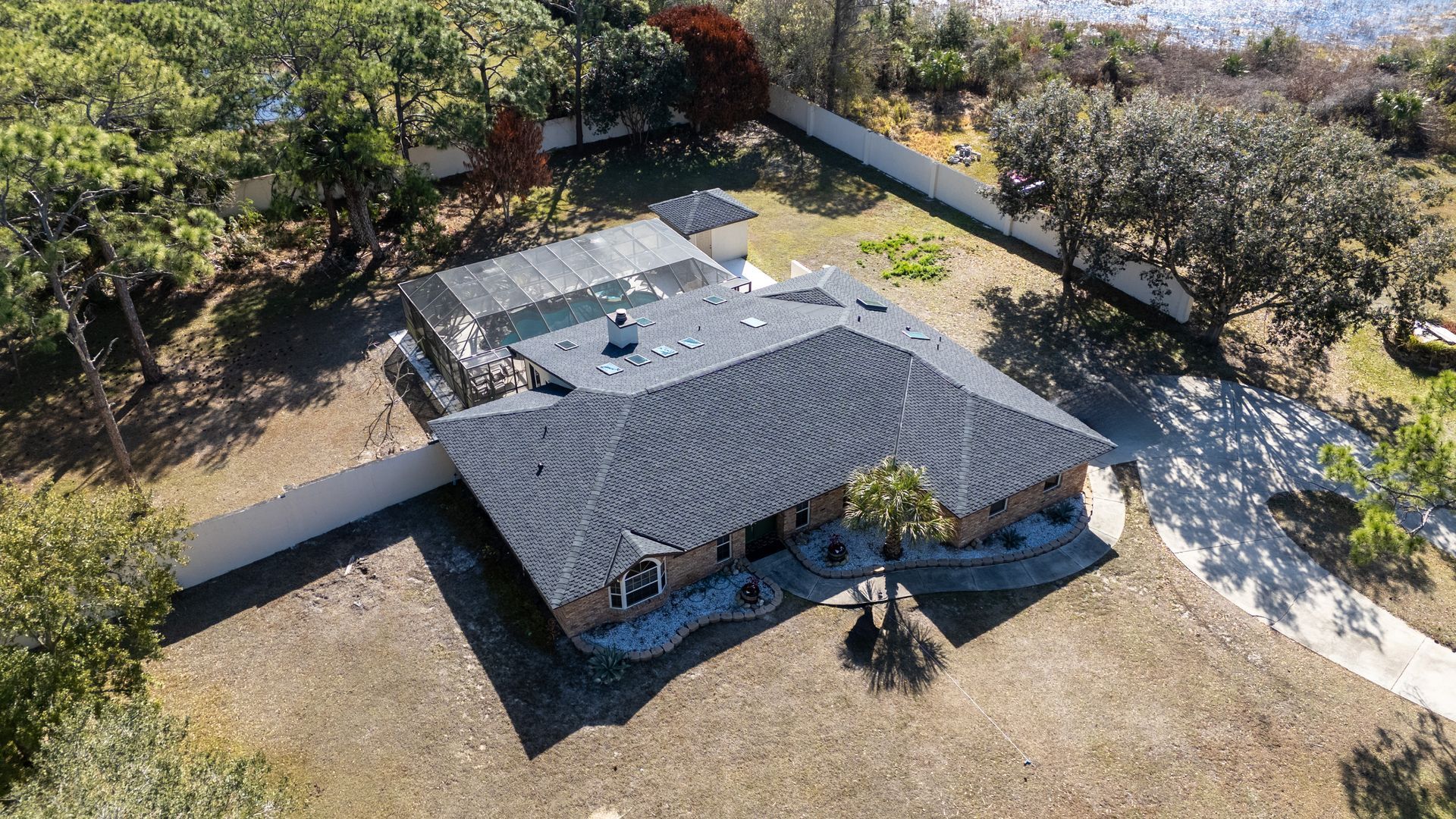 An aerial view of a single-story house with a grey shingled hip roof, a white front door, and a concrete driveway.