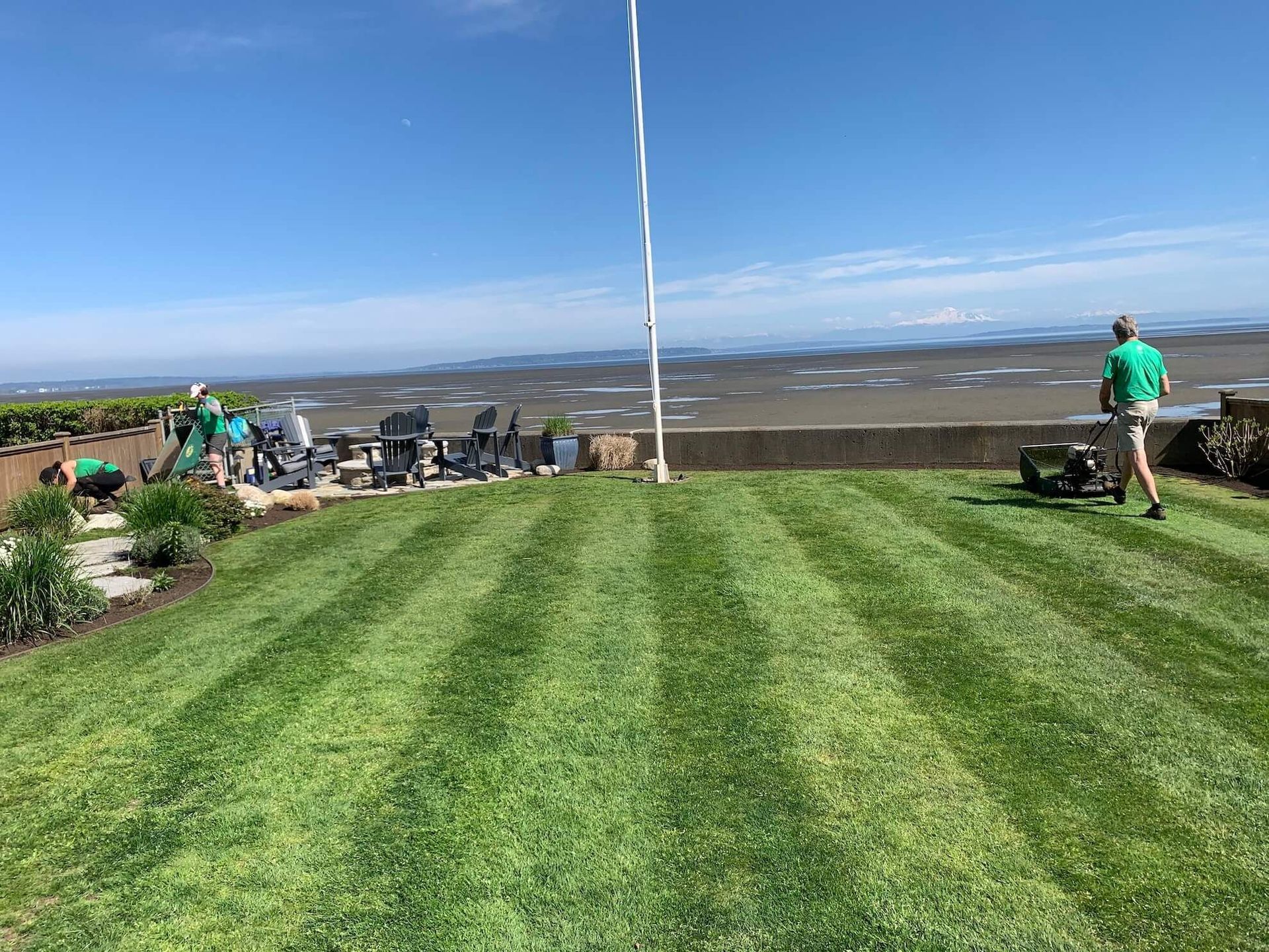 A man is mowing a lush green lawn with a view of the ocean.