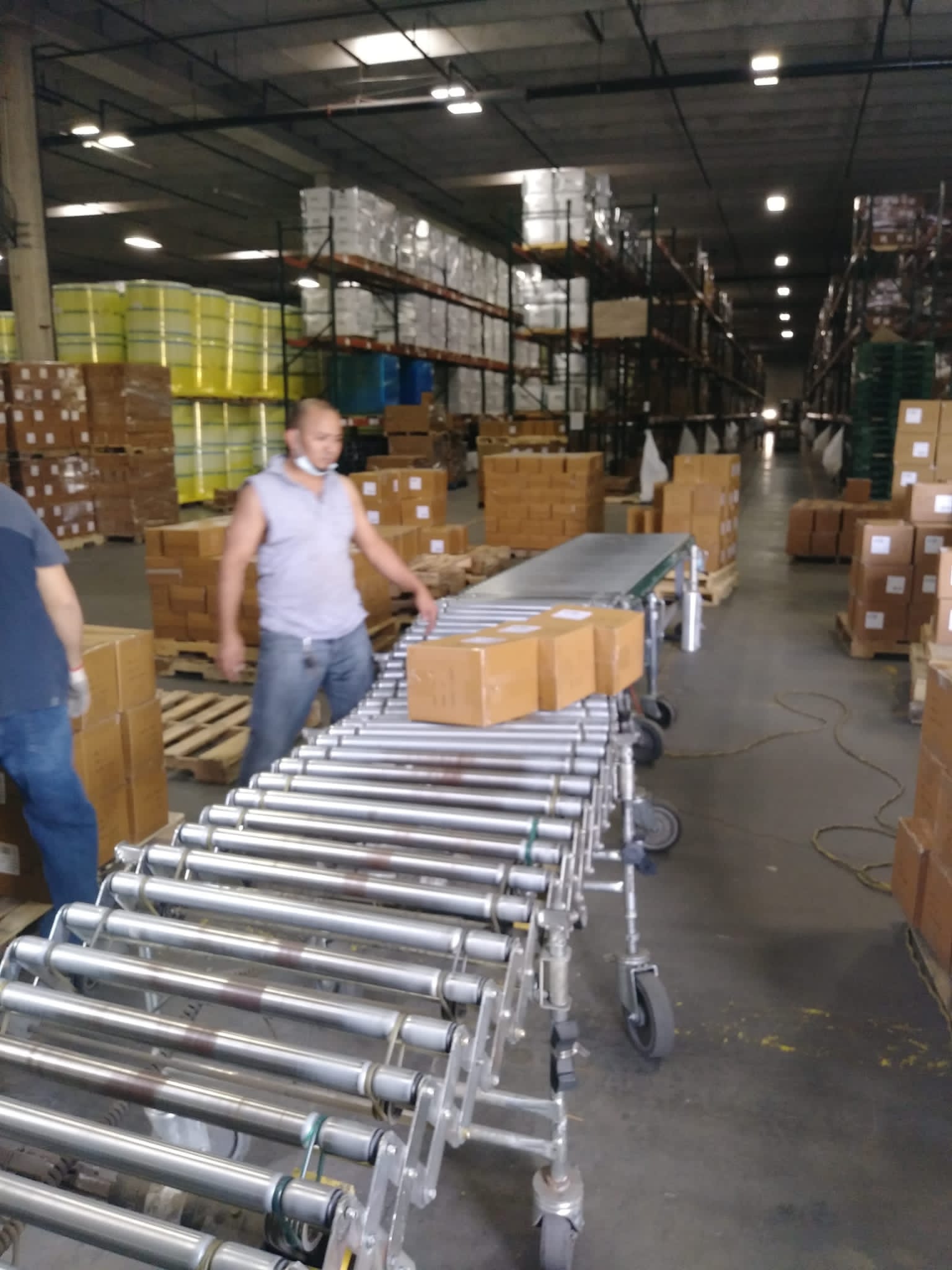 Man in a warehouse sorting boxes on a conveyor belt; boxes and shelves filled with supplies.