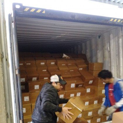 Two people unloading cardboard boxes from a shipping container.