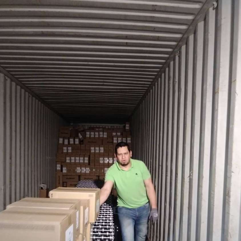 Man in green shirt and jeans inside a shipping container, loading boxes.