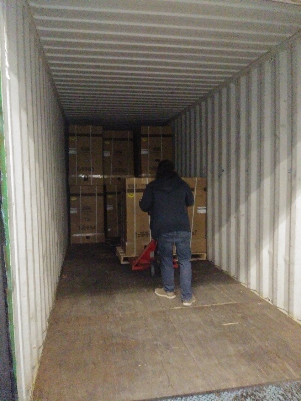 Person loading boxes on a pallet jack into a shipping container.