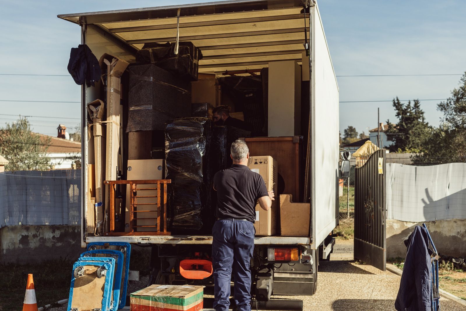 Man loading a moving truck with furniture and boxes in a driveway.