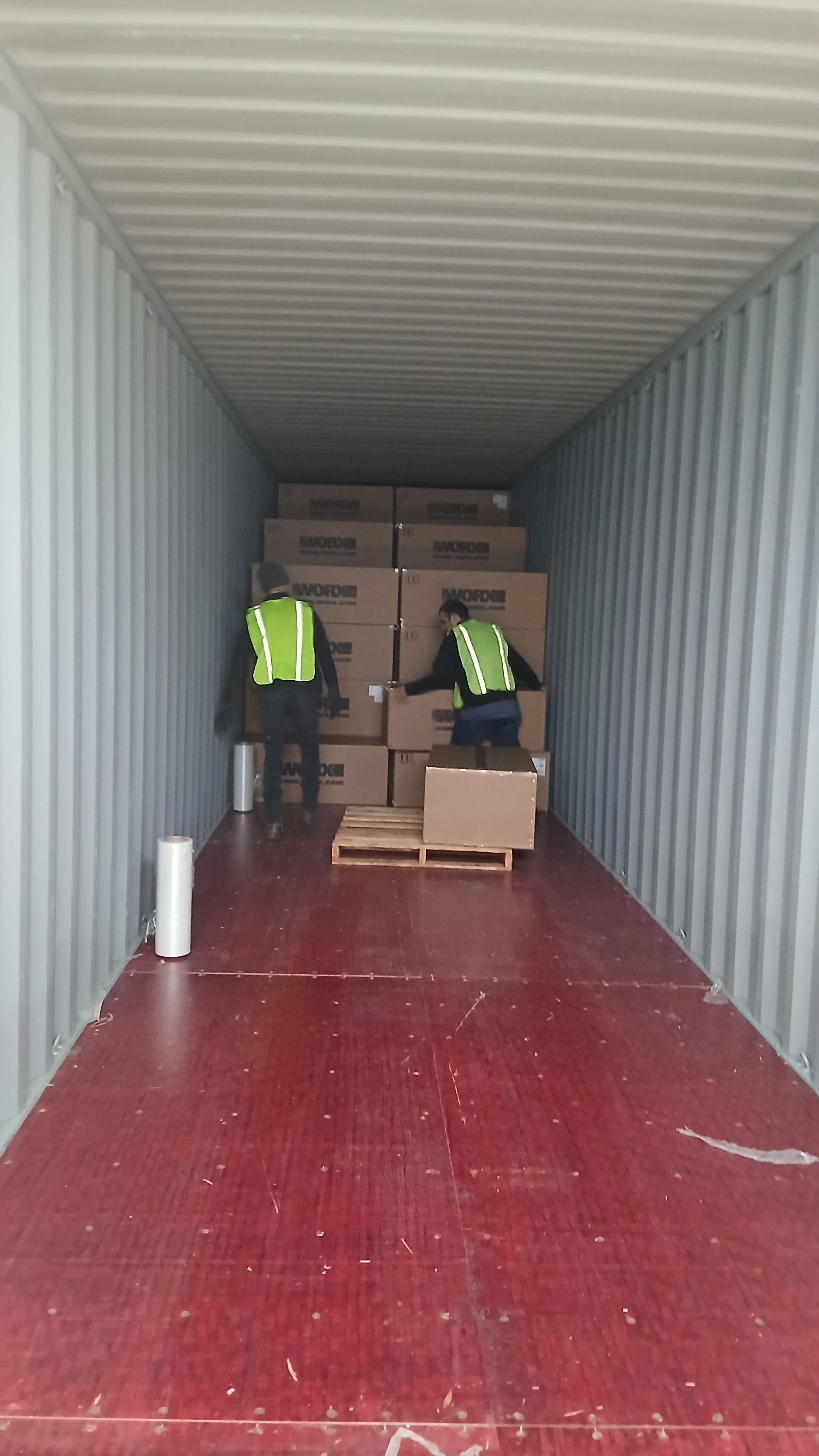 Two workers in safety vests loading boxes inside a shipping container.