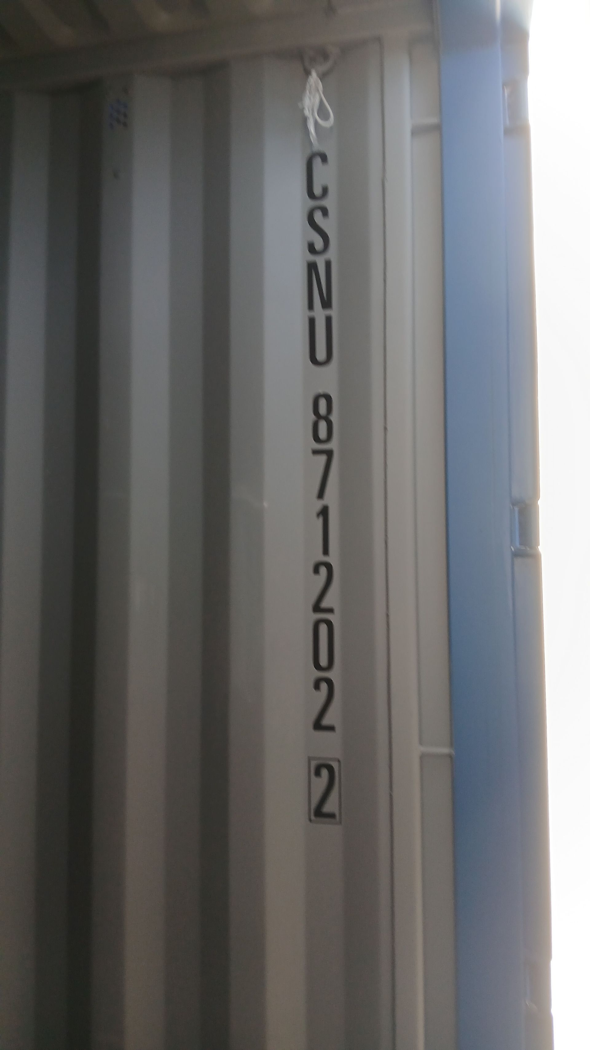 Container markings: CSNU 871202 2, vertically aligned on a corrugated gray metal wall, with a blue metal frame on the right.