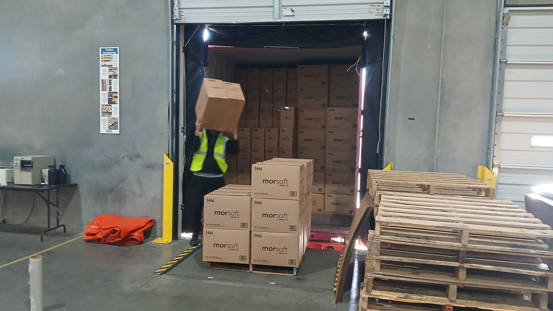 Warehouse worker in a safety vest carrying a cardboard box, loading a truck.