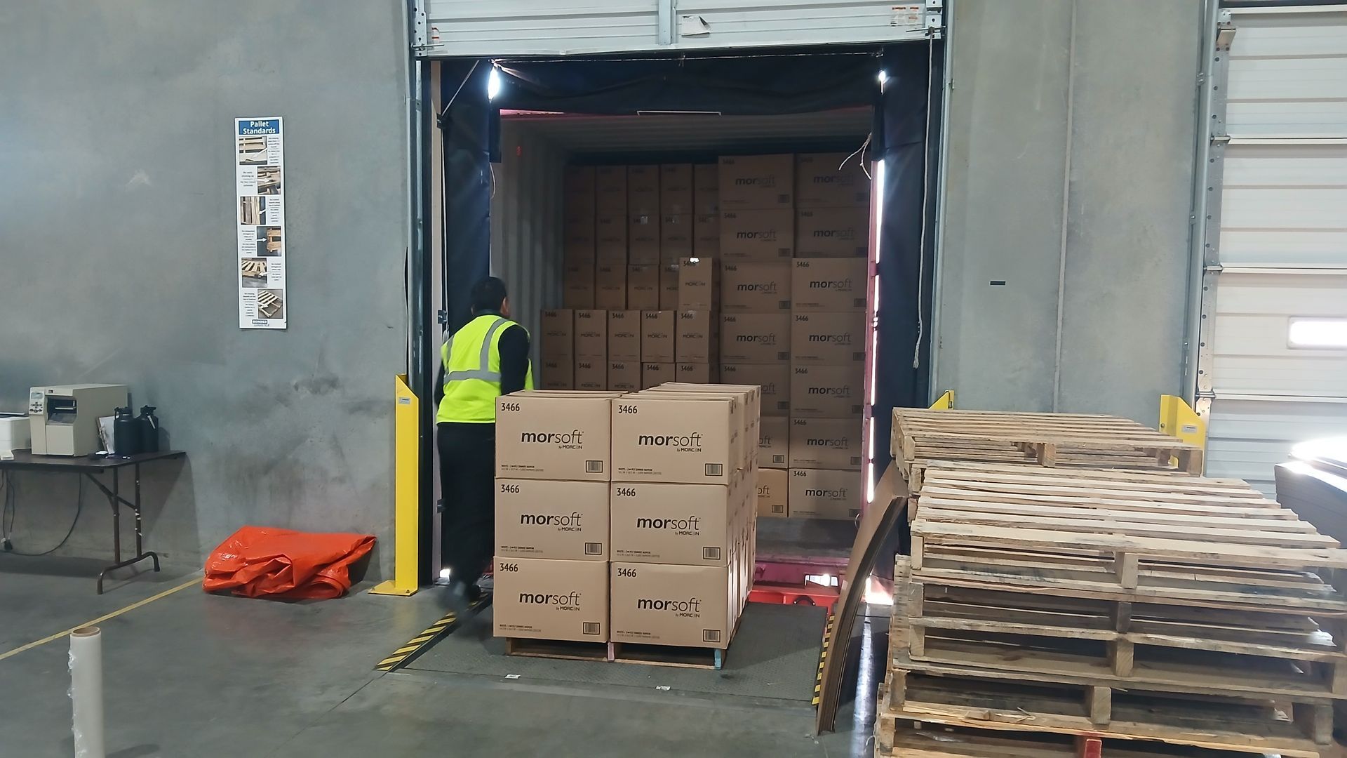 Worker in reflective vest loading boxes onto a truck at a loading dock.