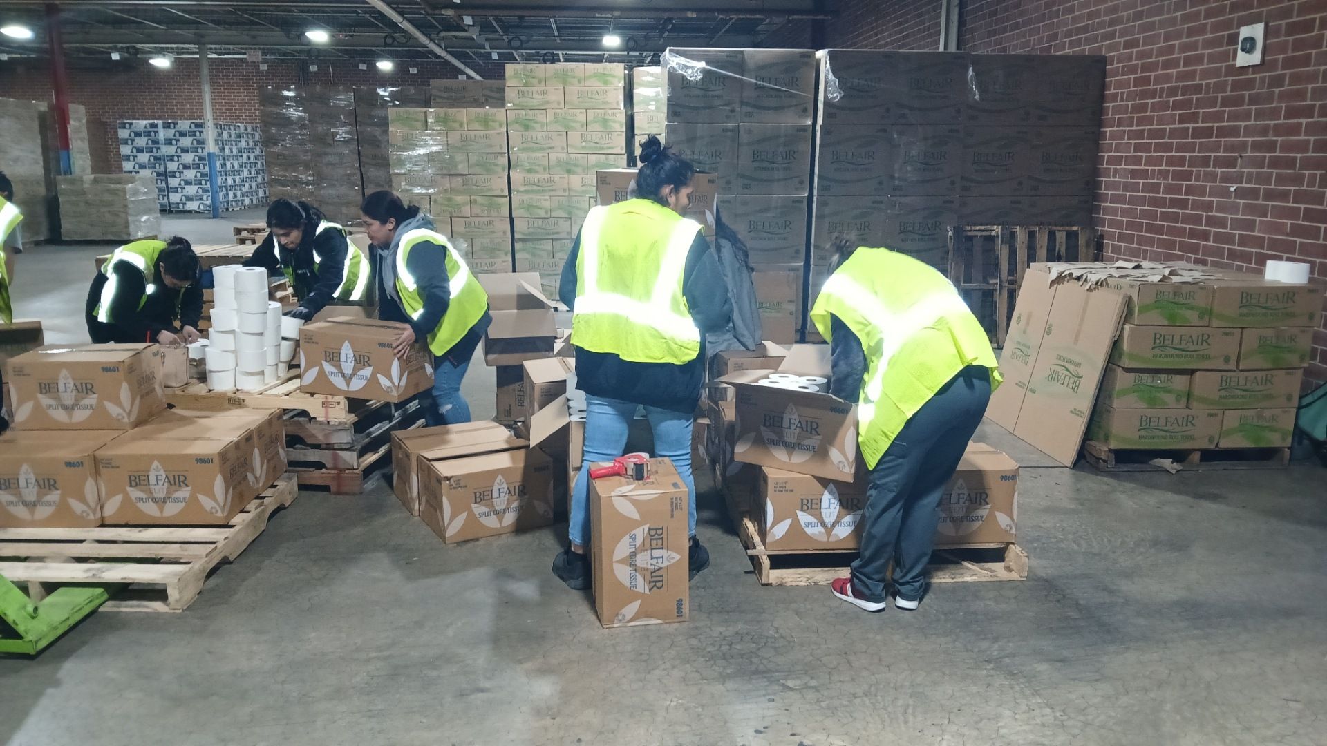 People in yellow vests packing boxes in a warehouse, likely for donation or distribution.