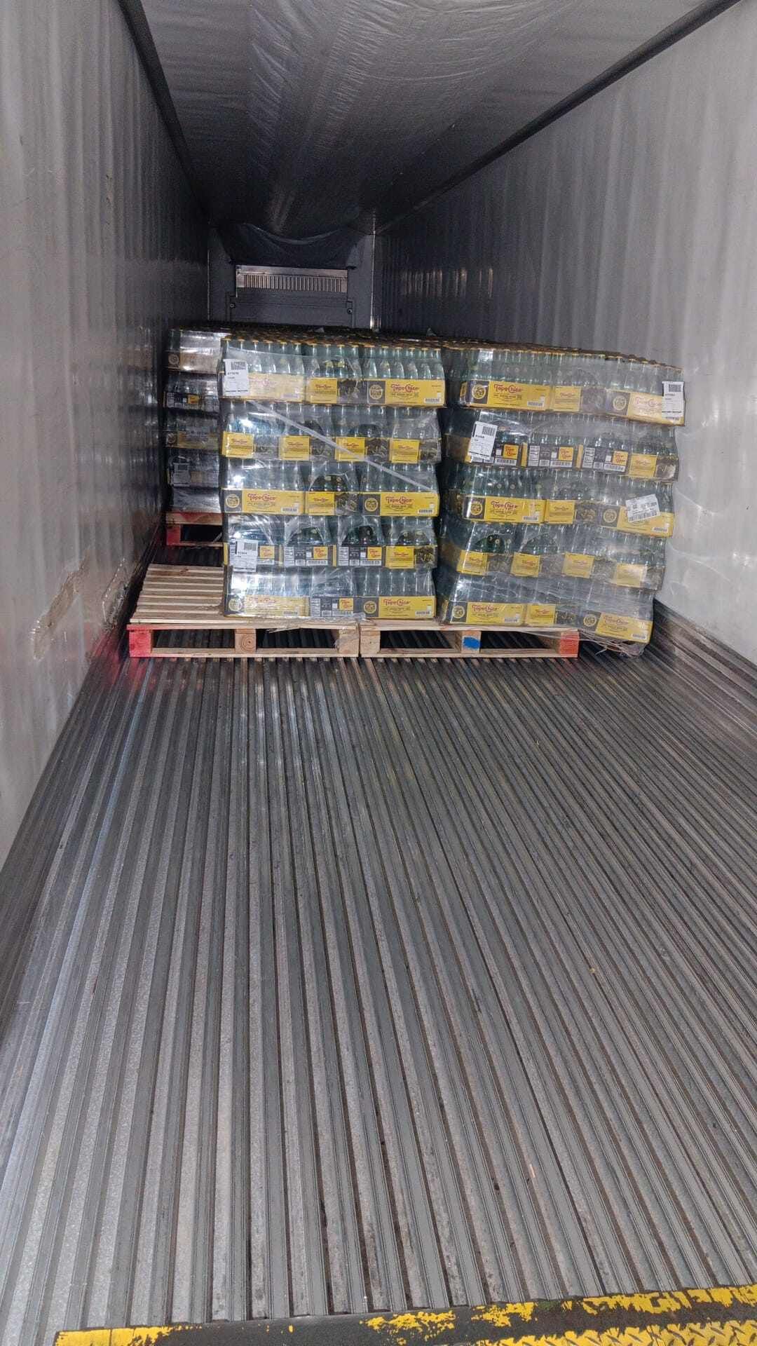 Inside a semi-trailer: Pallets of packaged goods wrapped in plastic, stacked on a corrugated metal floor.