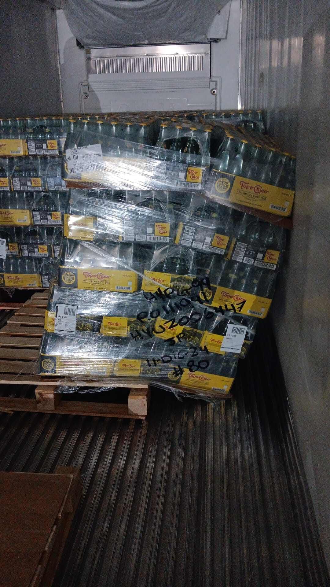 Pallet of water bottles leaning inside a refrigerated truck, wrapped in plastic.
