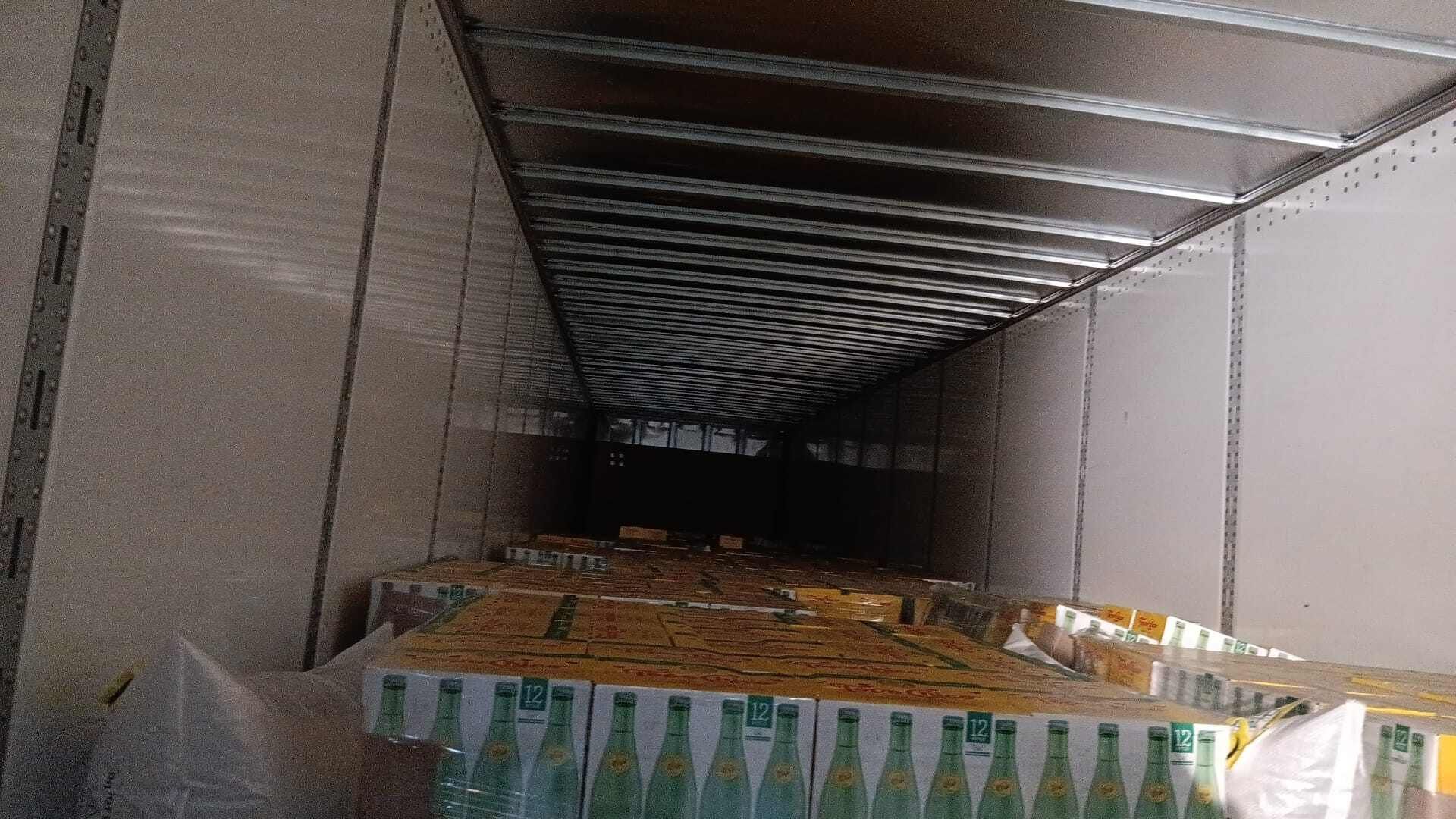 Inside of a semi-truck trailer, filled with boxes, looking down a long aisle.