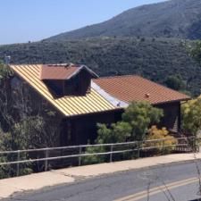 A house with a yellow roof is sitting on top of a hill next to a road.