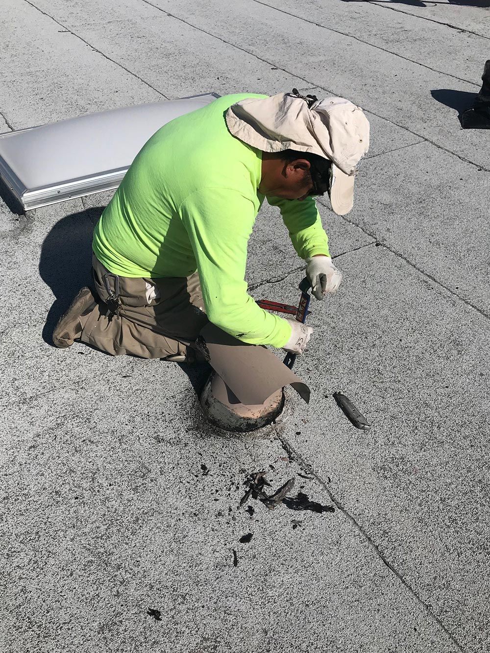 A man in a green shirt and hat is kneeling down on a roof.