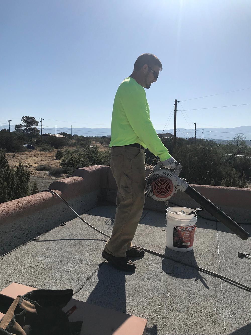 A man in a neon green shirt is working on a roof.