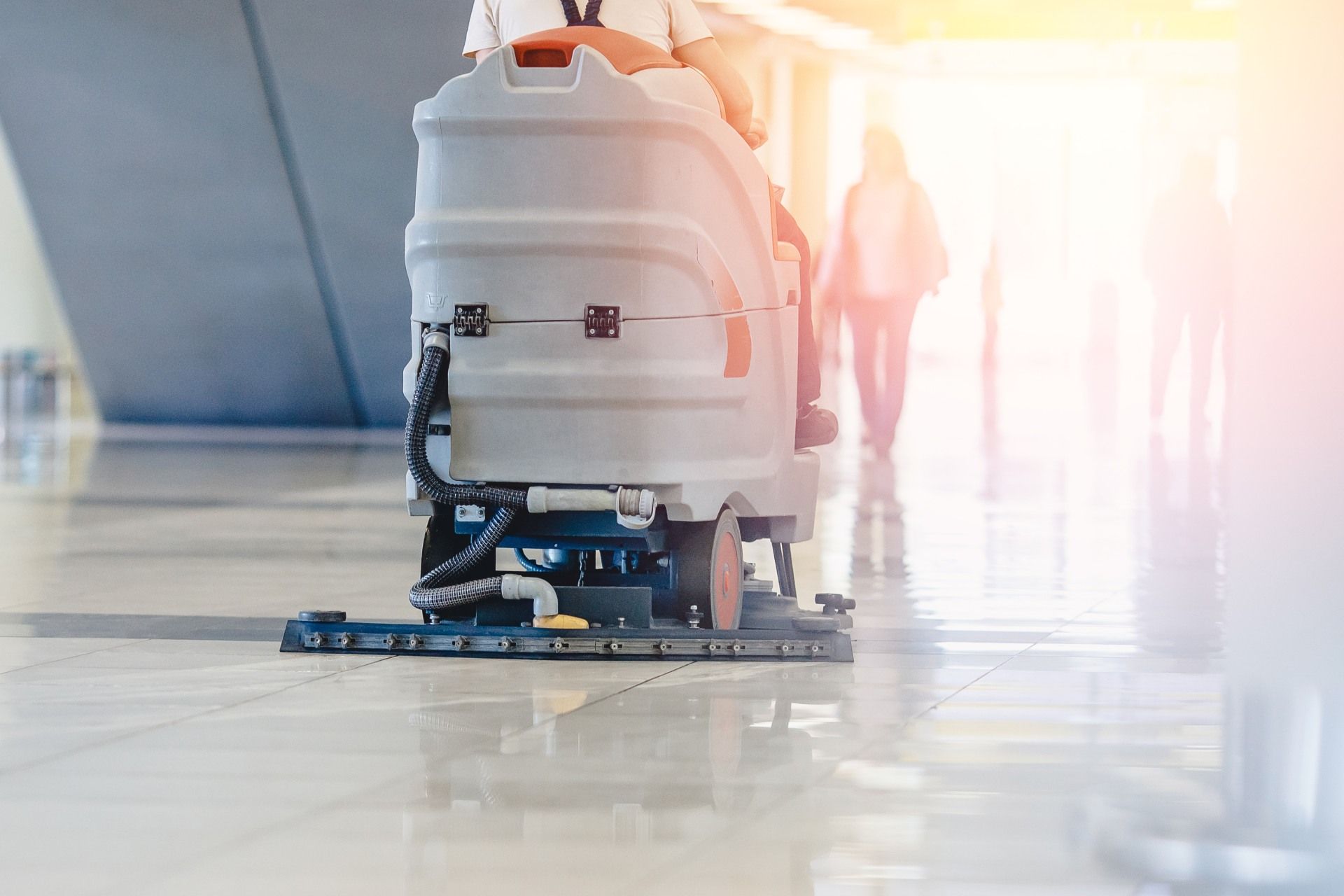 Floor cleaner machine operating on a shiny tiled floor; a person operates it indoors.