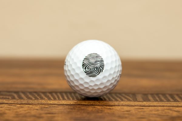 White golf ball with a fingerprint design, resting on a wooden surface against a neutral background.