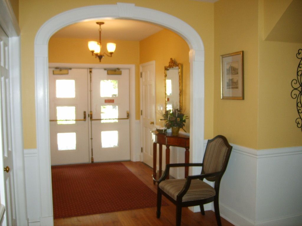 Yellow-walled interior with archway leading to doors. A chair and table sit in the hall.