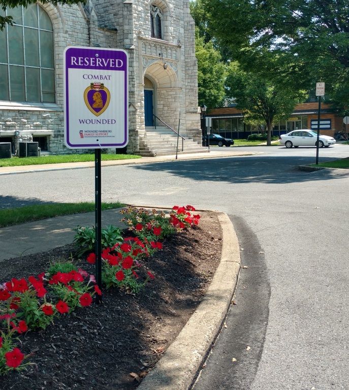 Purple Heart parking sign with red flowers in front of a building.