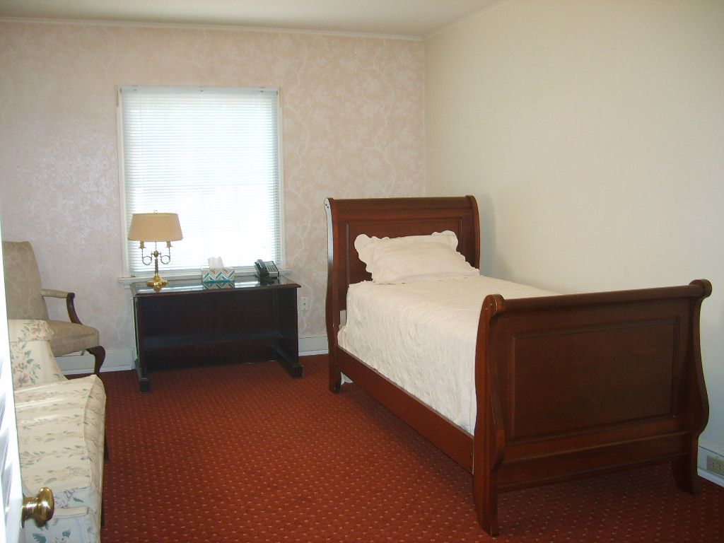 Bedroom with a twin bed, window, dark wooden desk, and red carpet.