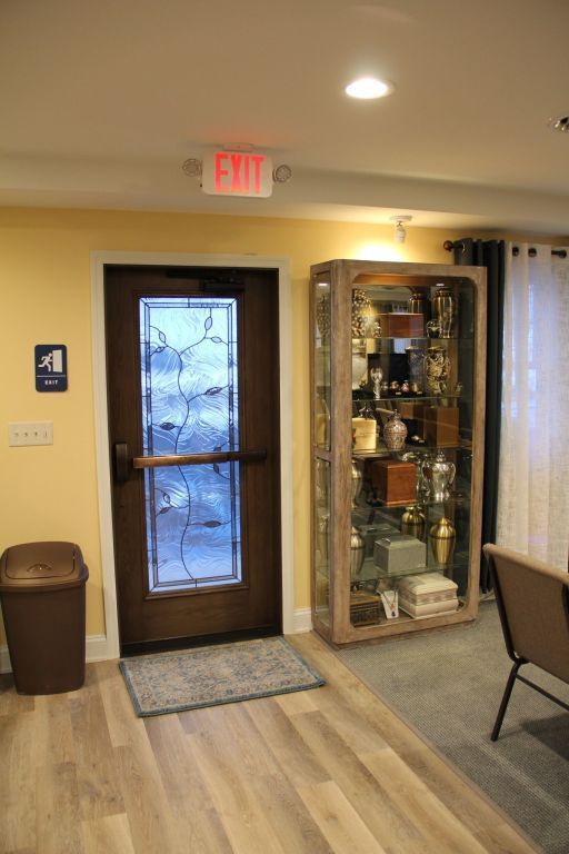 An interior shot showing an exit door with glass panel, a display case filled with items, and a bathroom sign. The room has light-colored walls and flooring.