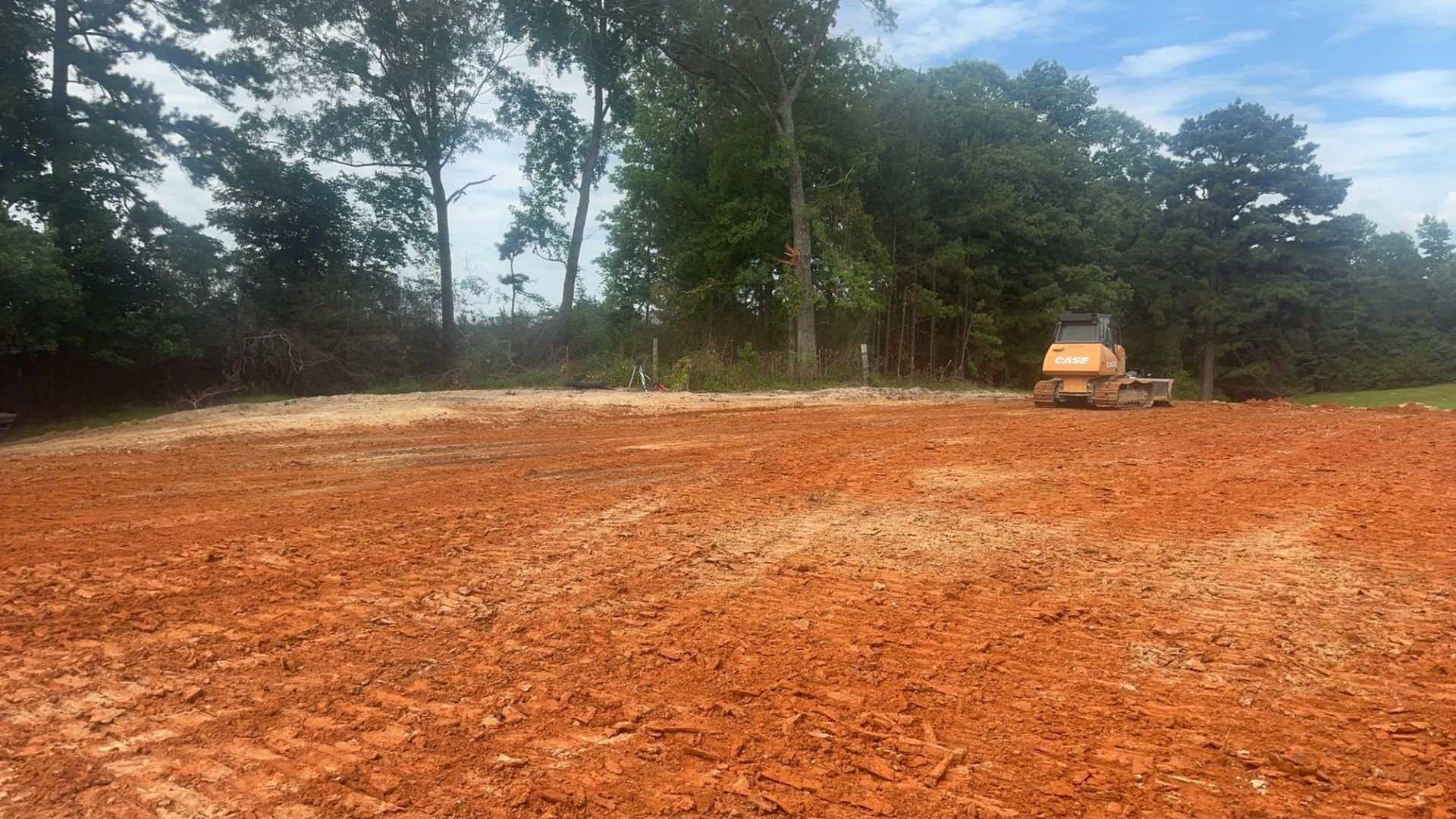Brown earth, cleared area. Small bulldozer works. Trees and blue sky in the background.
