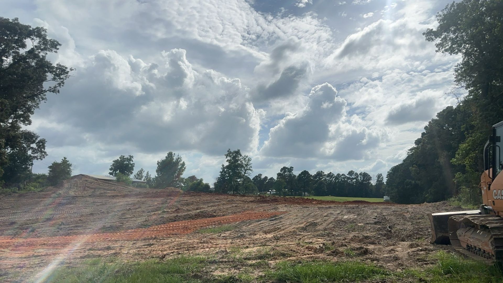 A bulldozer on a construction site, with piles of dirt and a cloudy sky overhead.