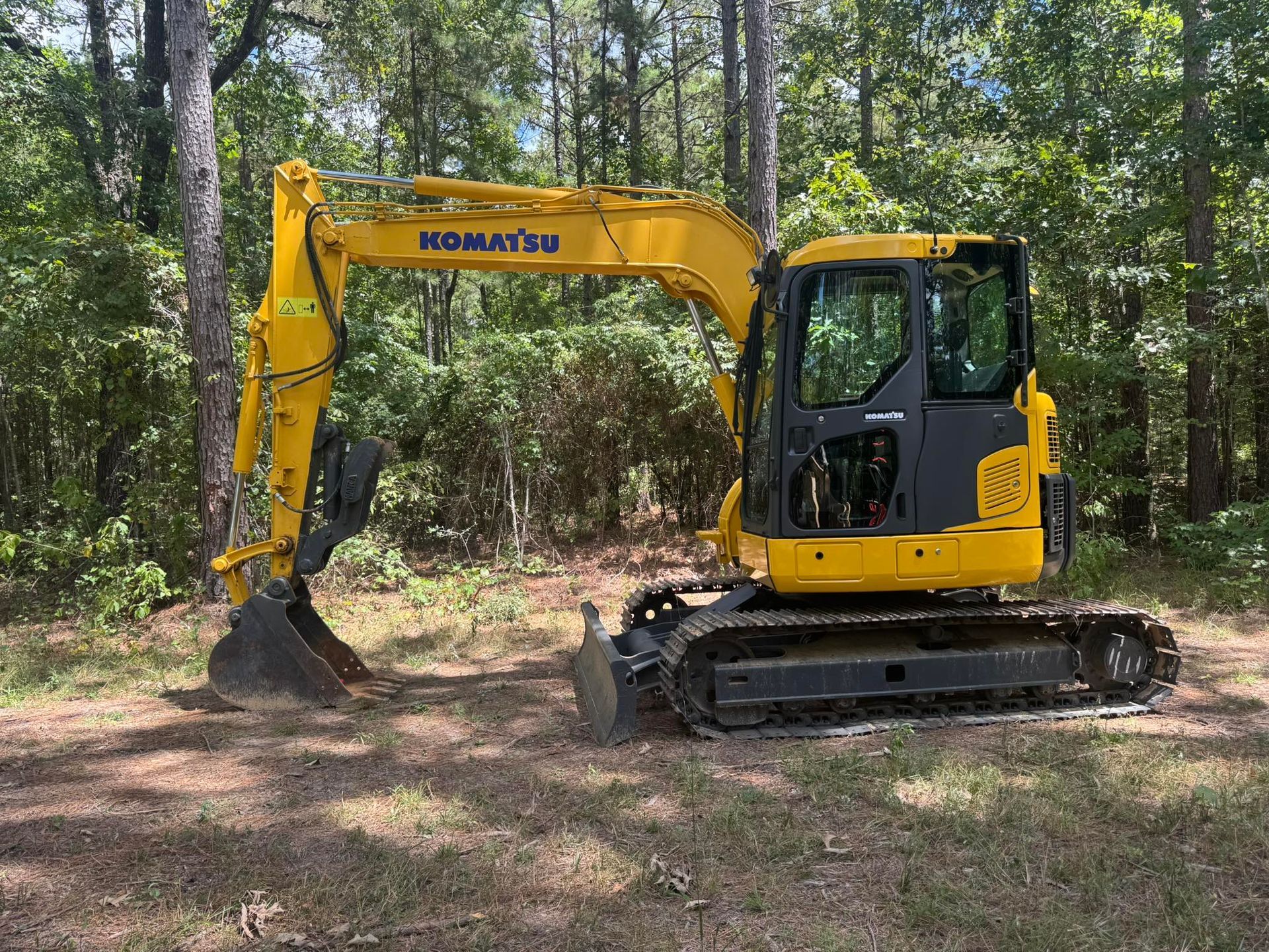 Yellow Komatsu excavator on tracks in a wooded area, ready for digging.