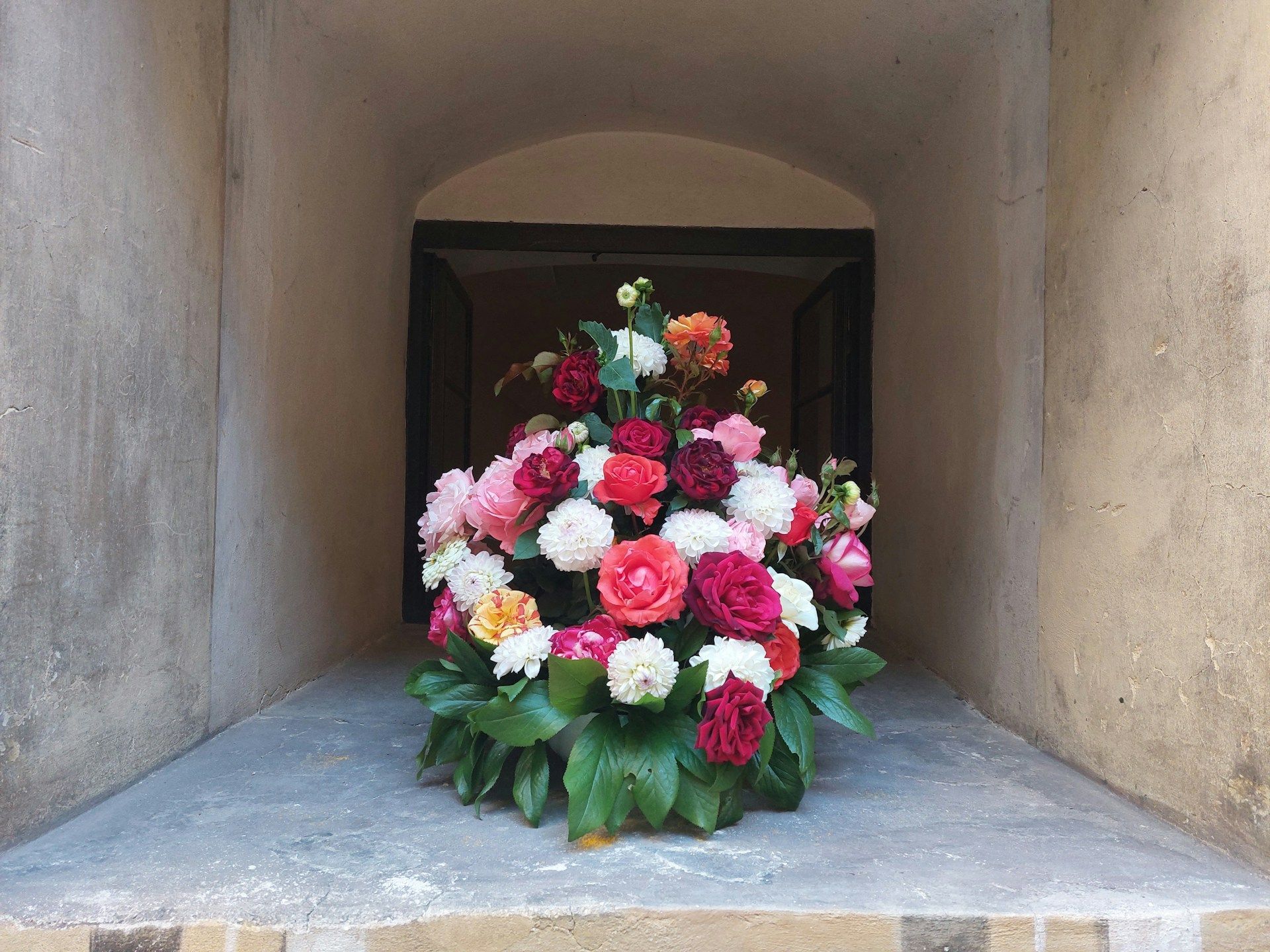 Colorful funeral flower arrangement with roses and peonies in shades of red, pink, and white.