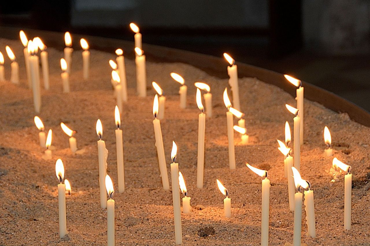 Group of lit memorial candles in a church setting casting soft light symbolizing remembrance.