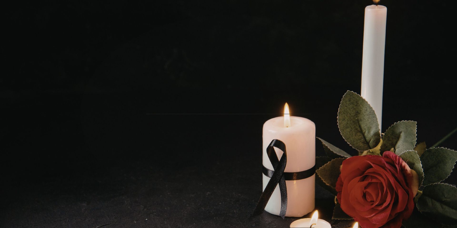 Lit memorial candles with a black ribbon and red rose on a dark background, symbolizing remembrance,