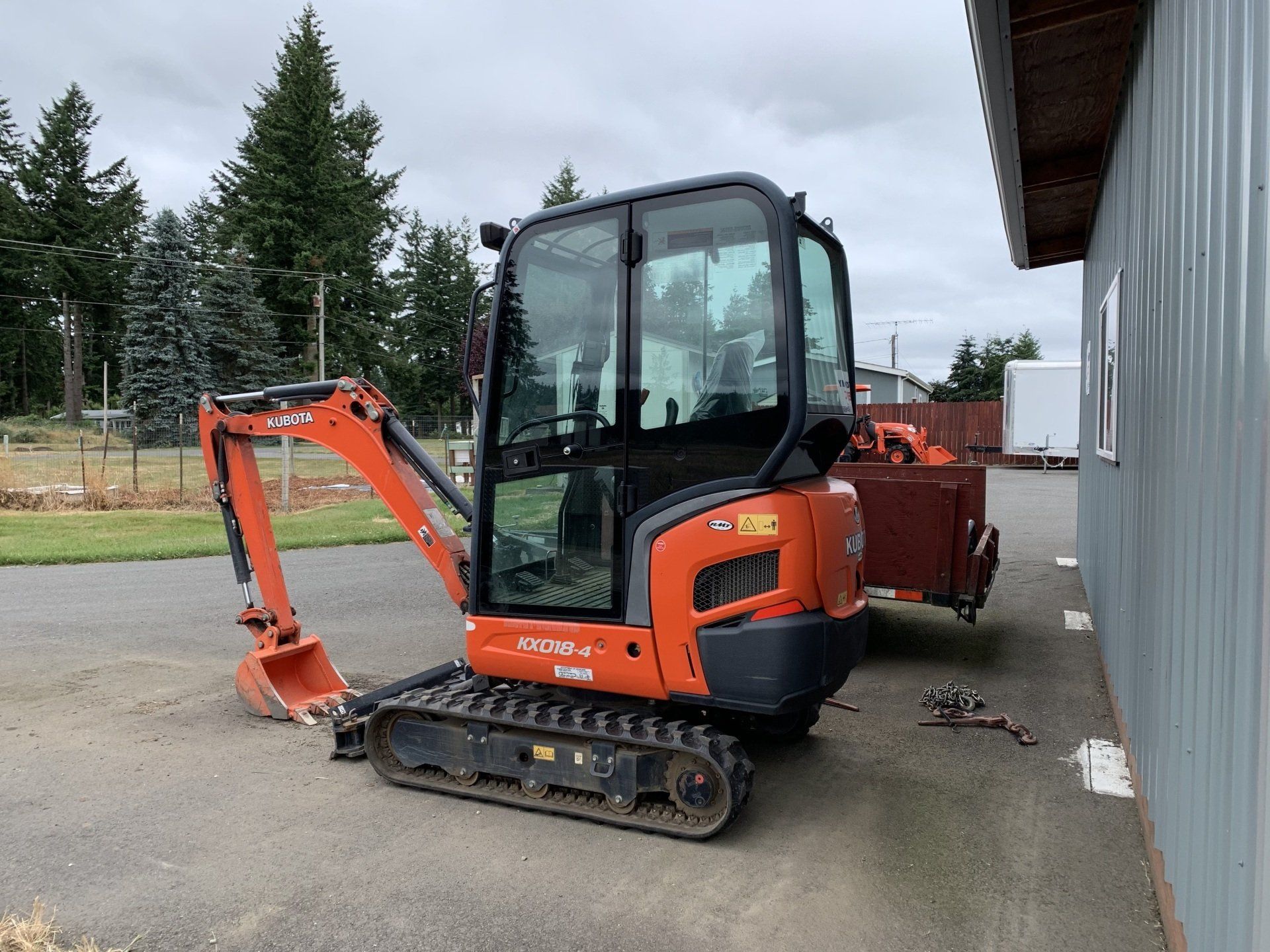 Orange Kubota excavator parked beside a gray building on a cloudy day.