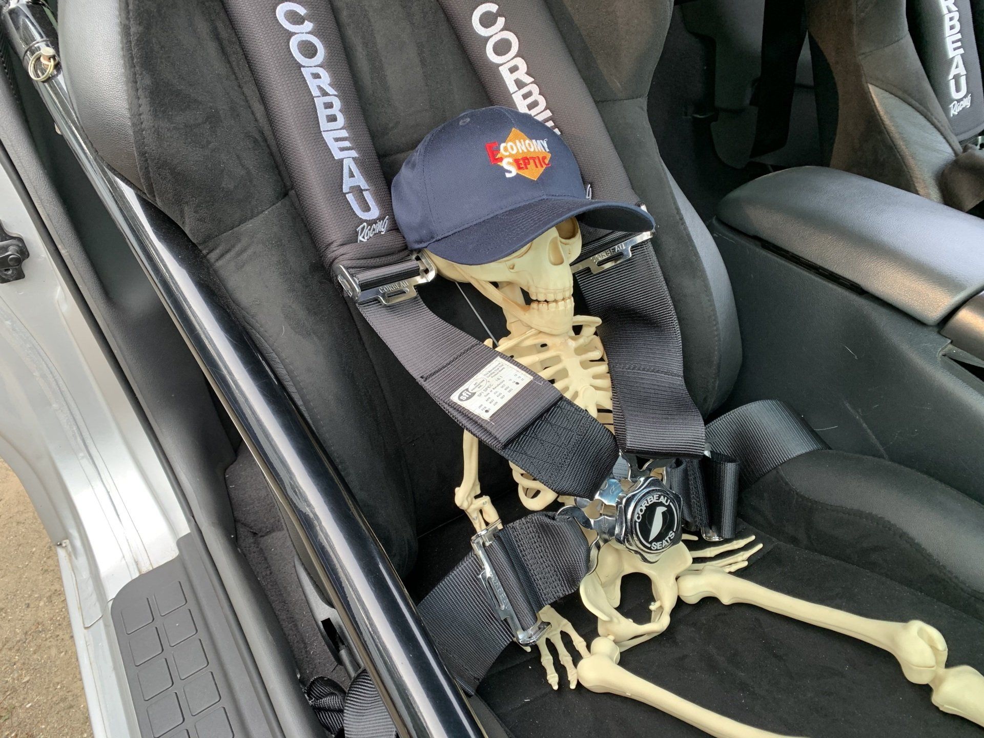Skeleton wearing a hat, strapped into a racing car seat.
