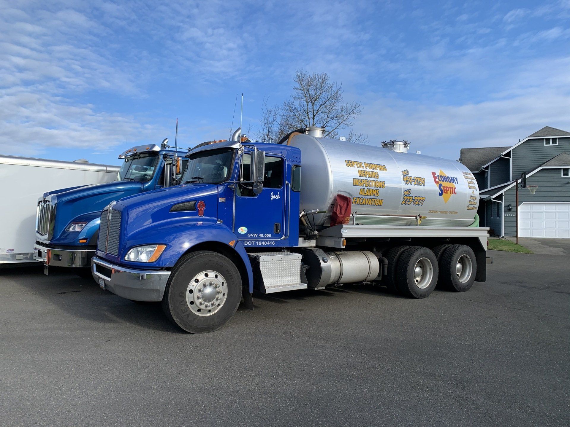 Blue tanker truck parked in a lot with other trucks and houses in the background.
