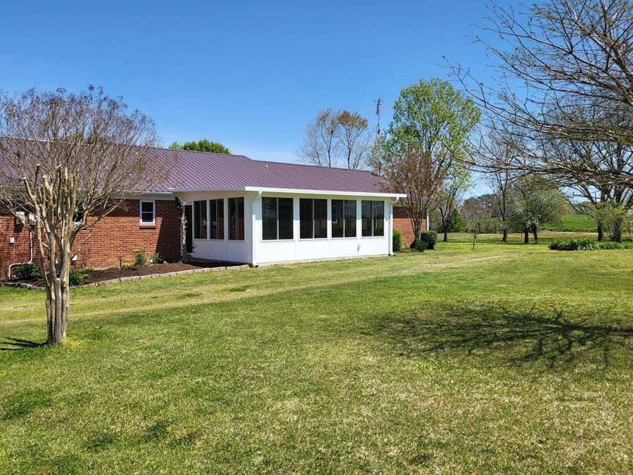 A house with a screened in porch and a large lawn in front of it
