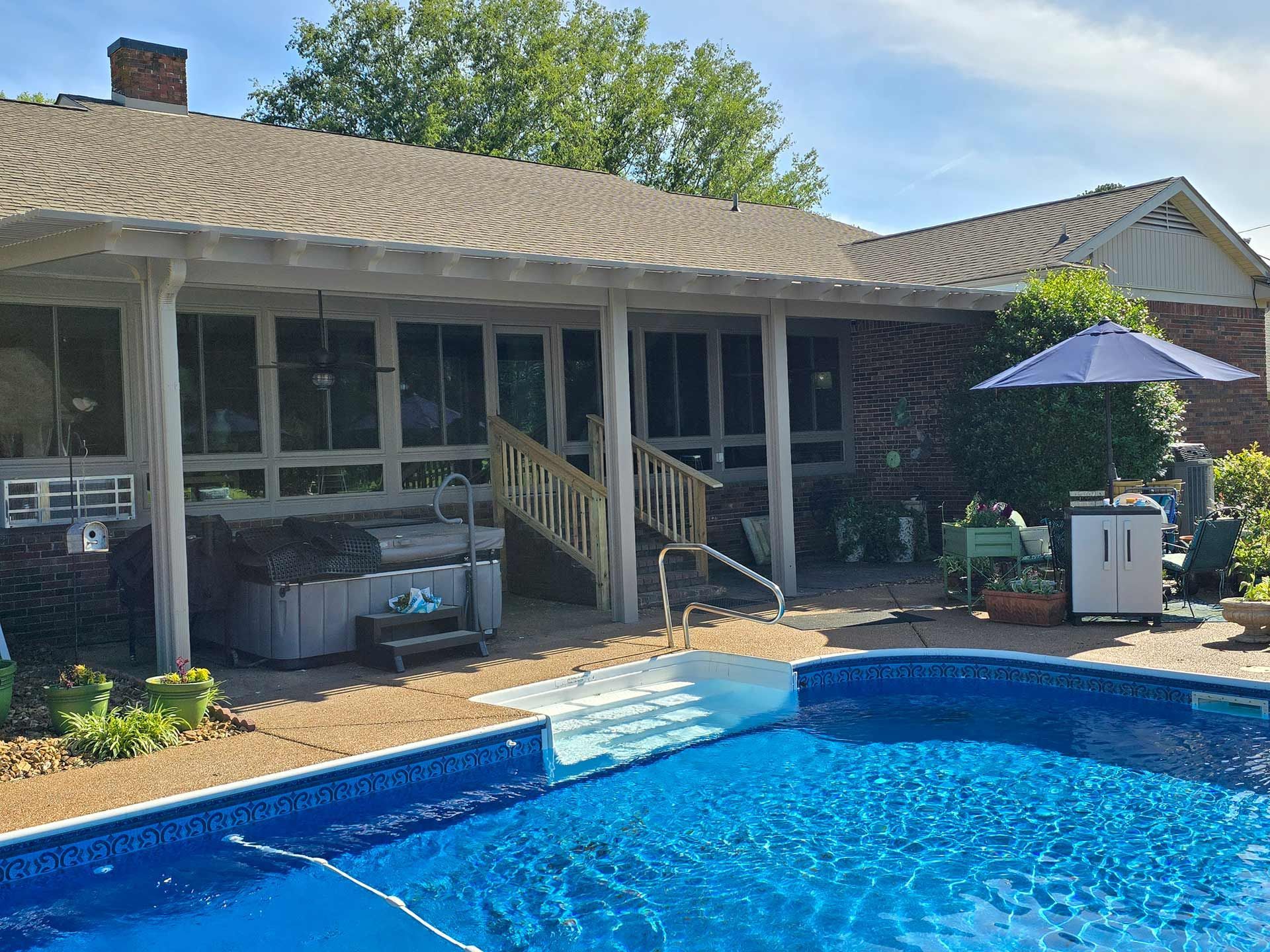 A large swimming pool is in front of a house with a screened in porch