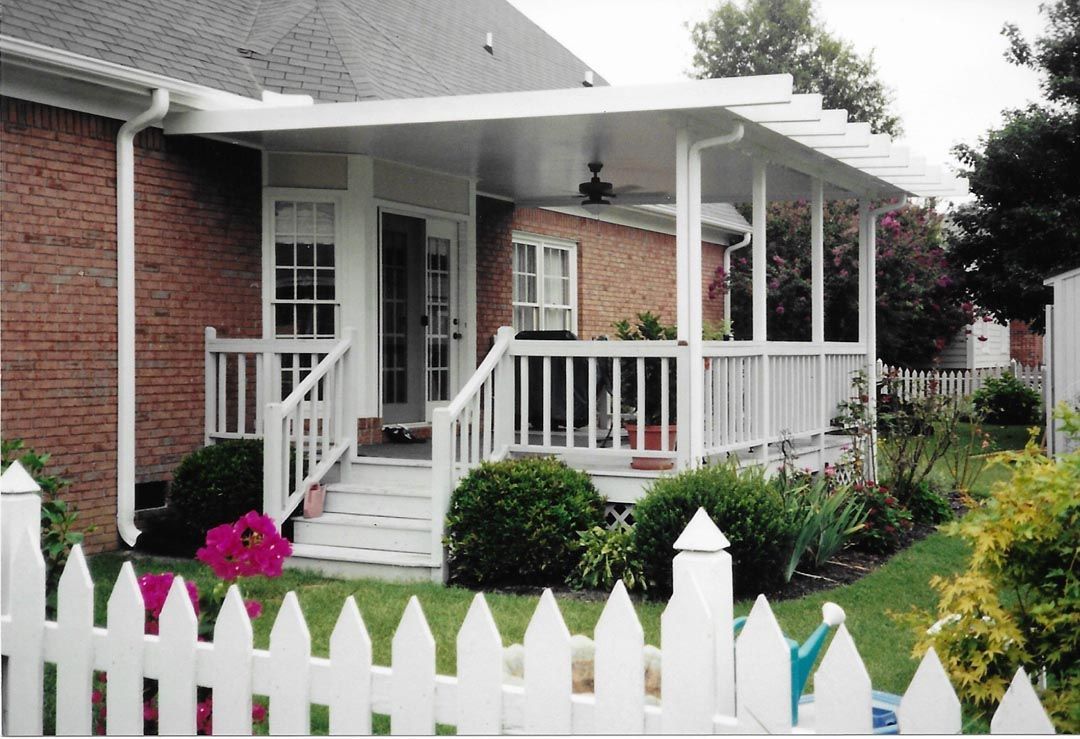 A white picket fence surrounds a brick house with a porch