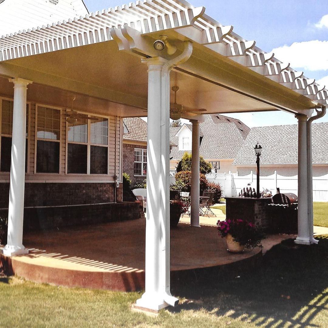 A patio with a pergola and white pillars in front of a house