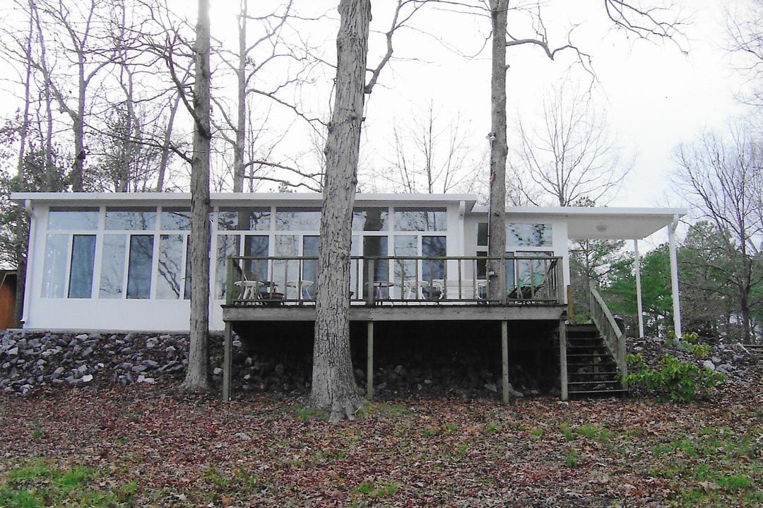 A white house with a large deck is surrounded by trees