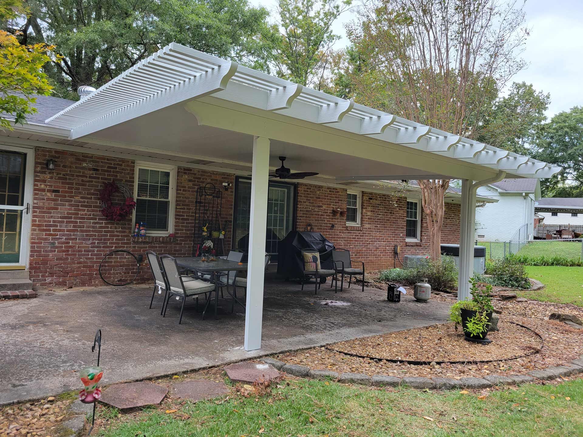 A white pergola is sitting on top of a patio in front of a brick house