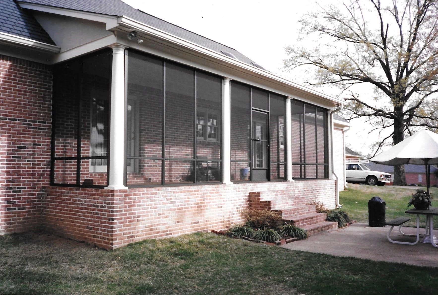 A screened in porch on the side of a brick house