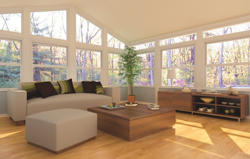 A living room with a couch , coffee table , ottoman and lots of windows