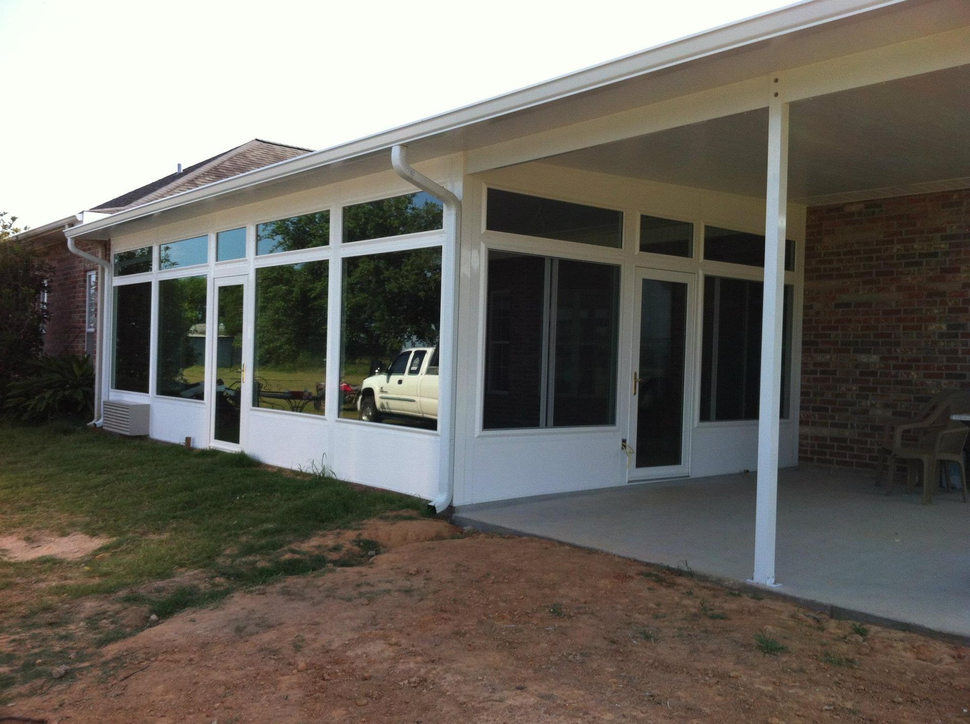 A white truck is parked in front of a house with a screened in porch