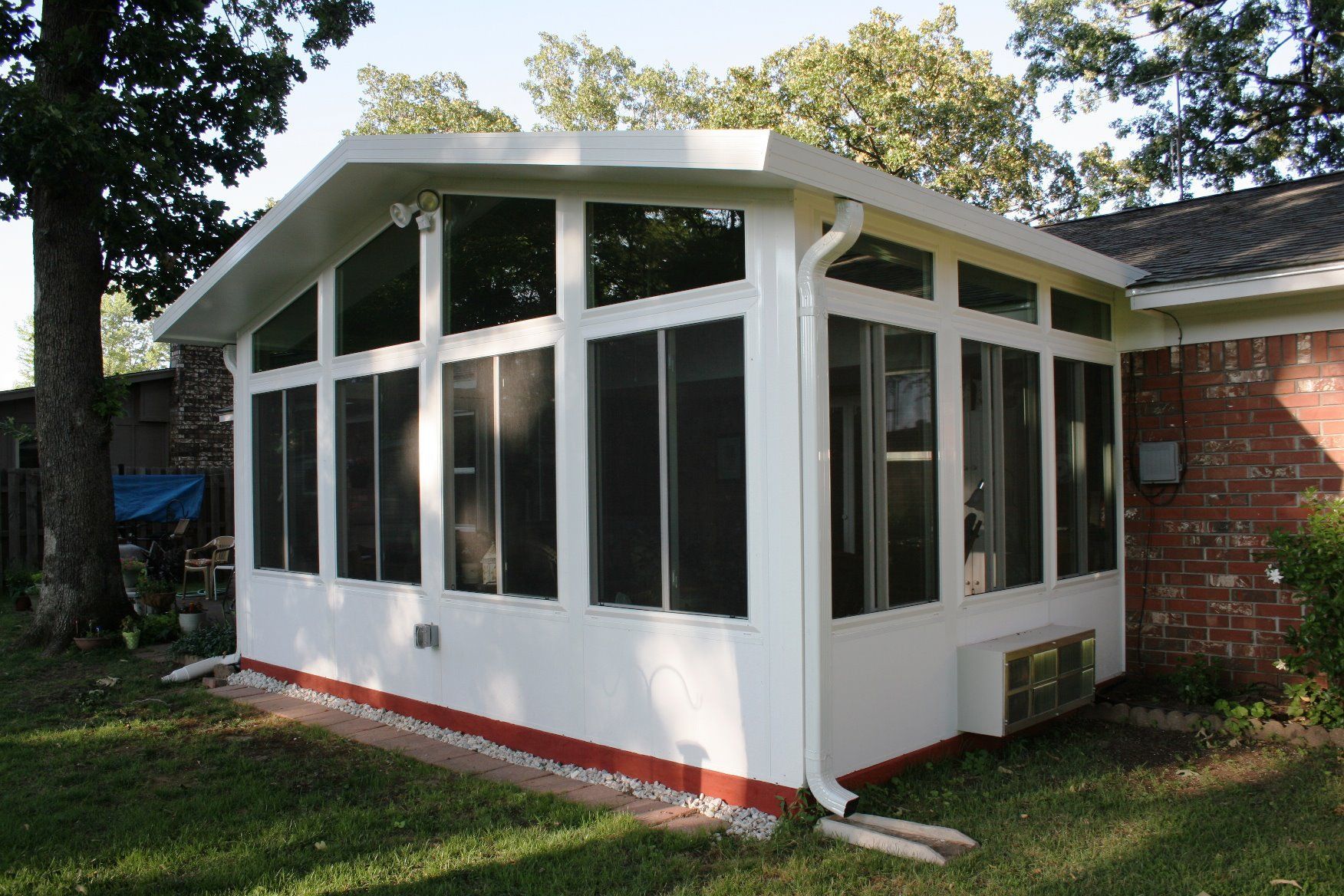 A white screened in porch is sitting in the backyard of a brick house