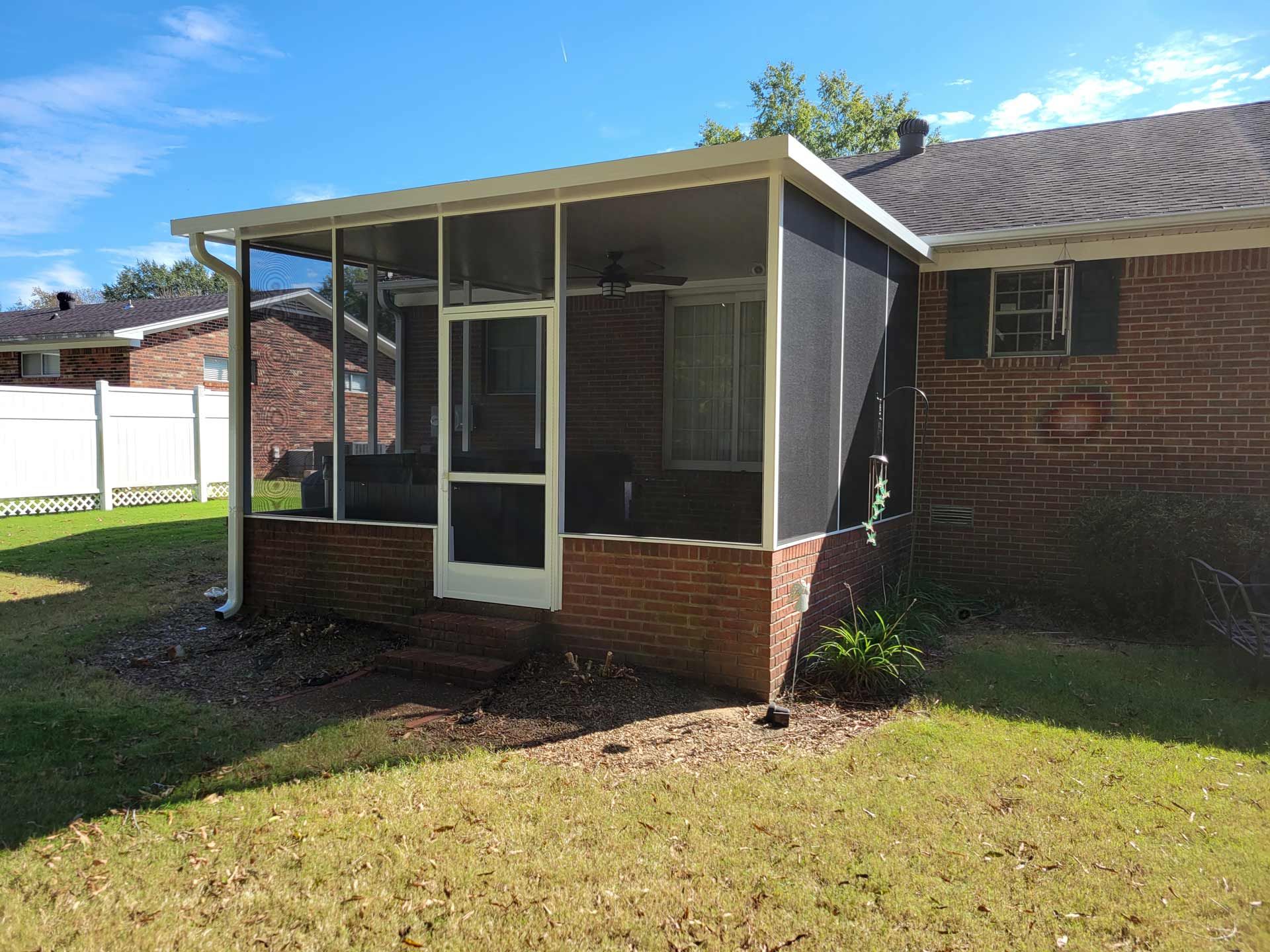 A screened in porch with a brick house in the background